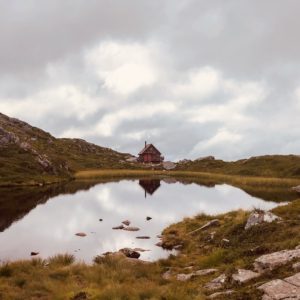 Cabin on green grass field near lake under white clouds