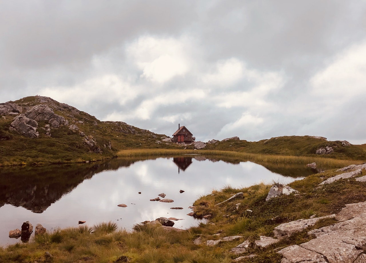 Cabin on green grass field near lake under white clouds