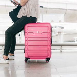 Woman in white top and denim jeans sitting on red luggage