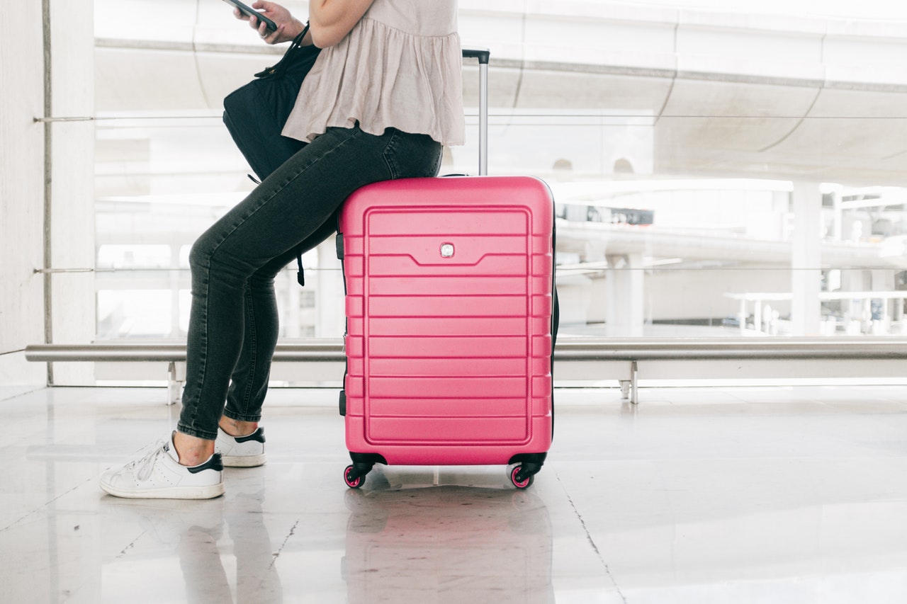 Woman in white top and denim jeans sitting on red luggage